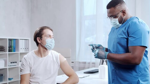 African-American doctor makes a coronavirus vaccine using a syringe and hypodermic needle. Medical worker and patient at the hospital office. Vaccination and safety concept.