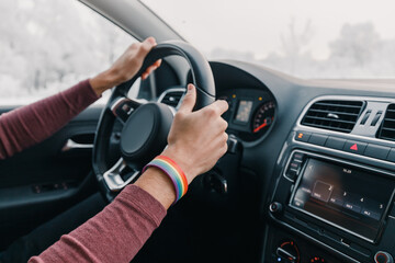 The driver's hand on the steering wheel with a rainbow bracelet as a symbol of LGBT movement. The concept of a road trip and immigration