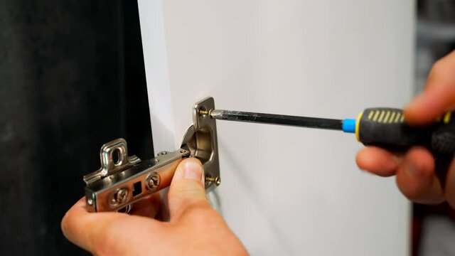 The cabinet maker tightens the adjustment screw on the cabinet door hinge in the kitchen. Installation and adjustment of cabinet doors.