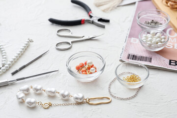 Workplace of jewelry designer with  tools and beads on light background