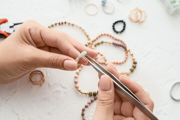 Female designer making jewelry on light background