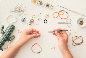 Female designer making jewelry on light background