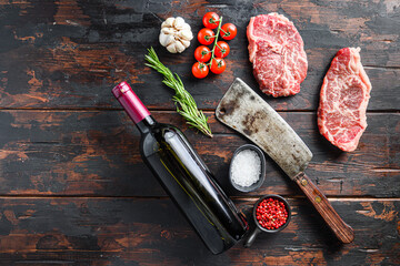 Top blade organic meat cut, raw marbled beef steak, with old butcher knife cleaver, red wine bottle  and seasonings  On dark wooden rustic table,  top view with space for text.