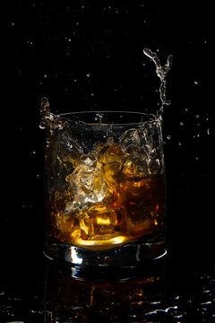 glass of scotch whiskey with splash and ice on black background