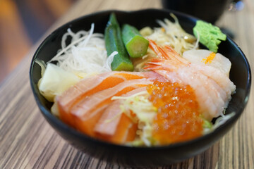 Fresh raw seafood mixed rice bowl. Japanese Rice with sashimi of salmon, scallop, okra and ikura (Salmon eggs) on a wooden table.