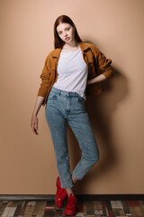 Girl in jeans and a brown jacket posing on a beige background