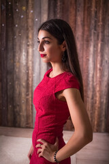 woman model in elegant red dress. Beautiful girl studio shot on wooden background. Brunette posing holding a lock of hair in her hand