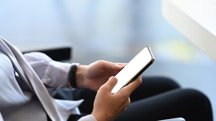 Close up view of casual asian woman using mobile phone while sitting on a chair at her workspace.