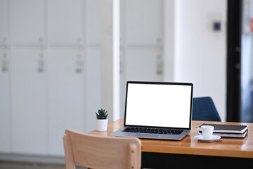 Mock up laptop computer with white screen on wooden table in modern office.