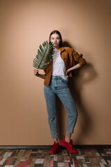 Girl in jeans and a brown jacket posing on a beige background