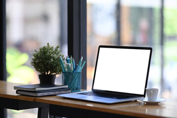 Simple workspace with laptop computer mock up, office supplies and plant decoration on desk.