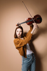 Girl in jeans and a brown jacket plays the violin on a beige background