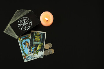 Tarot card 5 pentacle and The World cards next to a deck of cards and 5 silver coins. With a white candle lit With a black space on the left to write a message.