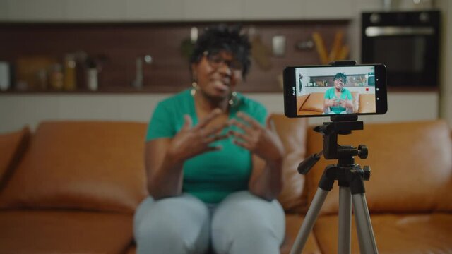 Positive attractive senior african american female blogger recording video content for vlog on cellphone, sharing with online audience life hacks and long time experience. Focus on smart phone screen.