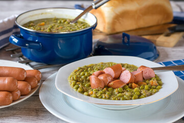 Plate and pot of fresh cooked peas soup with sausages