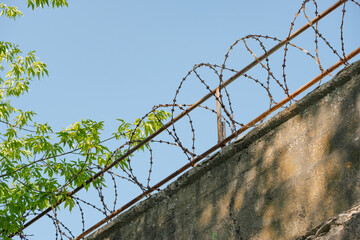 concrete wall of a prison with a fence at the top with barbed wire