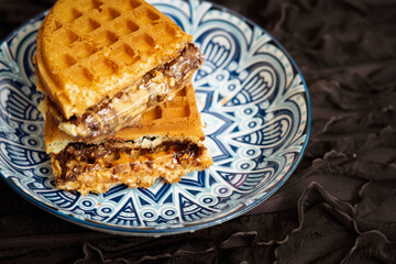 Fresh waffles with peanut butter and chocolate spread on a decorated plate.