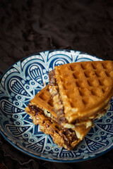 Fresh waffles with peanut butter and chocolate spread on a decorated plate.