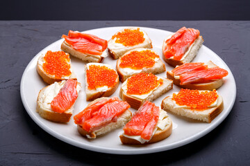 Bruschettes with butter and trout on a white plate on a gray background.