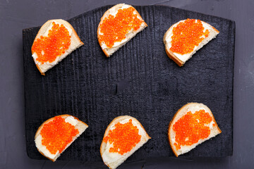 Bruschettes with butter and red caviar laid out on a black board on a gray concrete background copy space.
