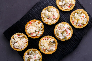 Tartlets with salad on a black wooden board on a gray concrete background.