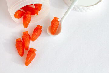 a bottle of gummy vitamins with carotene on white background; top view of chewing carrot form supplement, copy space