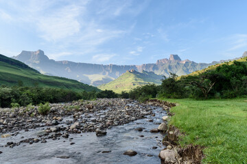Tugela river and the Amphitheater Drakenberg Mountains in the Royal Natal Nature Reserve in South Africa during green summer with a partial cloudy sky.