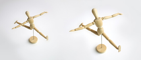A wooden doll is dancing ballet doing splits and raising its hand up. Isolated on white background.