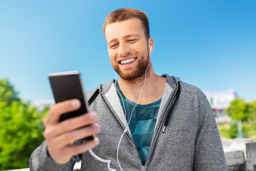 Obraz na płótnie Canvas fitness, sport and technology concept - happy smiling young man with earphones and smartphone listening to music outdoors