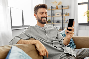 technology, internet, communication and people concept - happy smiling young man texting on smartphone at home