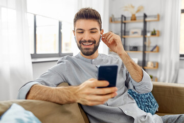 technology, leisure and people concept - happy man in earphones with smartphone listening to music at home