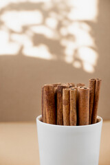 cinnamon sticks in a glass on a beige background. savory spices for cooking. Monochrome food photography, selective focus, vertical image with shadow