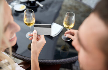 people, payment and finances concept - close up of couple at restaurant, woman pays a bill with credit card