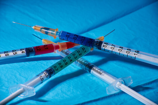 Jeringas con líquidos de diferentes colores sobre una tela quirúrgica simulando vacunas de diferentes orígenes trabajando juntas