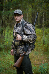 Man hunter standing with shotgun rifle outdoors preparing for bird hunt in autumn forest.