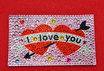 A beautiful picture of two red hearts made of shiny multi-colored stones with the inscription I love you on a red background. Valentine's Day or February 14