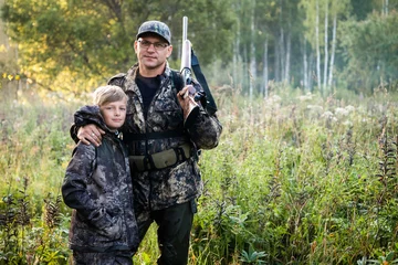 Fototapeten Father and son walking together outdoors with rifle for hunting © romankosolapov
