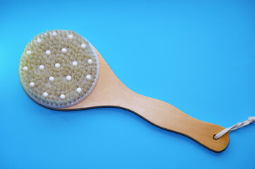 Wooden massage anti-cellulite shower brush with natural bristles on blue background with copy space