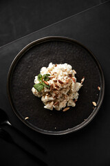 The vertical frame. Delicious dish of cauliflower, nuts, cream sauce and green mint leaves on a black plate, black table and black cutlery