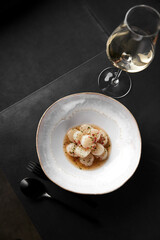 The vertical frame. Restaurant serving a delicious dish of scallop crudo and a glass of white wine on a black background