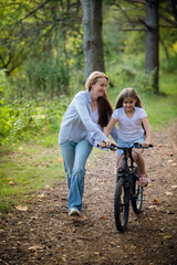 Obraz na płótnie Canvas Happy mother teaches his daughter to ride a bike