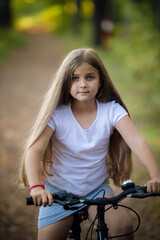 Fototapeta na wymiar Children girl riding bicycle outdoor in forest smiling.
