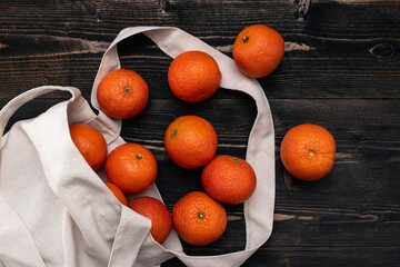 orange tangerine friuts tip out from white shopper bag on rustic wooden table surface