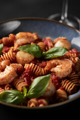 Vertical frame, a plate of delicious hot Italian pasta with seafood, shrimp, scallop and fresh basil on a black background with a glass of wine