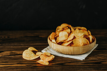 Potato chips in bowl on a wooden background. Salty crisps scattered on a table