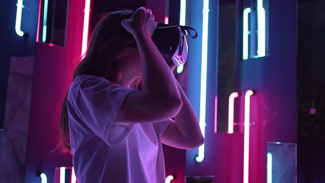 A woman put on virtual reality glasses. VR headset on neon background