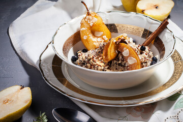 Vegan quinoa porridge with caramel, blueberries, sliced ​​pear, honey on a ladle in a bowl with ingredients above and a cloth napkin on a gray texture background. View from above. Healthy eating