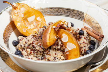 Vegan quinoa porridge with caramel, blueberries, sliced ​​pear, honey on a ladle in a bowl with ingredients above and a cloth napkin on a gray texture background. View from above. Healthy eating