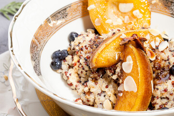 Vegan quinoa porridge with caramel, blueberries, sliced ​​pear, honey on a ladle in a bowl with ingredients above and a cloth napkin on a gray texture background. View from above. Healthy eating