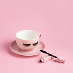 Cup of coffee with lashes and mascara on pastel pink background. Minimal make up concept. Make up as a lifestyle. Blogging workplace layout.